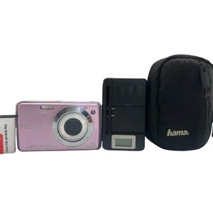 Peut inclure: Un appareil photo numérique Sony Cyber-shot rose, une batterie lithium-ion rectangulaire étiquetée NP-BG1, un chargeur de batterie universel noir avec un petit écran LCD et une housse de transport noire Hama à fermeture éclair.