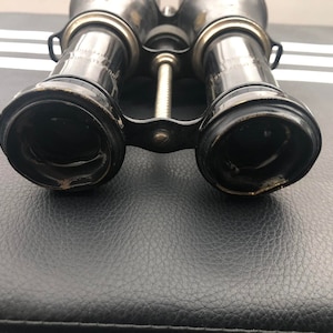 K&ouml;nnte beinhalten: Ein Paar vintage schwarze Ferngl&auml;ser mit silbernen Akzenten. Die Ferngl&auml;ser haben eine strukturierte Oberfl&auml;che und sind in gutem Zustand.