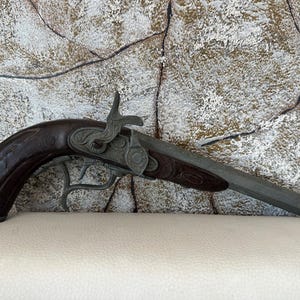 May include: A silver and brown toy pistol with intricate details. The pistol has a wooden handle and a metal barrel.