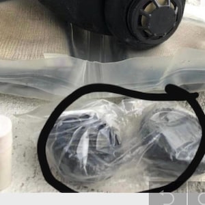 Puede incluir: Dos filtros de aire redondos negros de repuesto para una máscara de gas, empaquetados en una bolsa de plástico transparente.