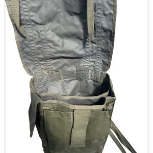 Può includere: Una borsa aperta in stile militare verde oliva con più scomparti e cinghie. La borsa è realizzata in un materiale resistente, possibilmente impermeabile. L'interno è visibile, mostrando la capacità di stoccaggio della borsa. La borsa ha una chiusura a patta e cinghie regolabili.