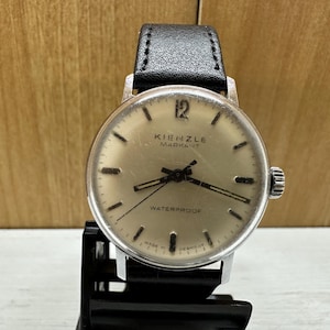 Könnte beinhalten: Eine silberne Kienzle Mark 17 Armbanduhr mit einem schwarzen Lederarmband. Das Zifferblatt der Uhr ist weiß mit schwarzen Zeigern und schwarzen Markierungen. Die Uhr ist wasserdicht.