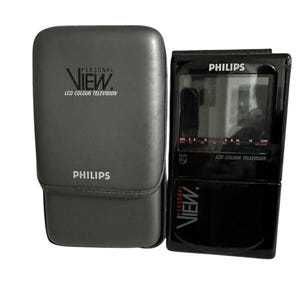 Puede incluir: Un televisor en color LCD Philips Personal View negro con una funda de transporte gris. El televisor tiene una pantalla pequeña y diales de selección de canales. La funda tiene el texto "PERSONAL VIEW" y "PHILIPS".