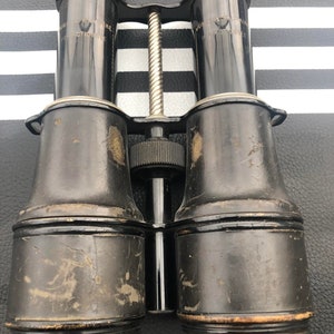 K&ouml;nnte beinhalten: Vintage-Fernglas aus schwarzem Leder mit einem silbernen Metall-Einstellknopf in der Mitte und dem Text "JUNIOR PANTOSCOPE" auf jeder Seite.