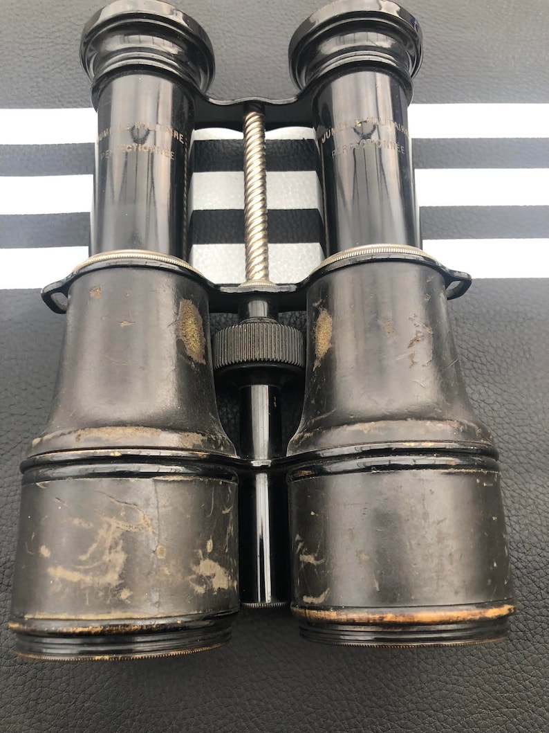 K&ouml;nnte beinhalten: Vintage-Fernglas aus schwarzem Leder mit einem silbernen Metall-Einstellknopf in der Mitte und dem Text "JUNIOR PANTOSCOPE" auf jeder Seite.