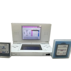 May include: A white Nintendo DS console with two game cartridges. The top screen shows a clock and calendar. One cartridge reads "THINK" and the other "PRACTISEENGLISH".