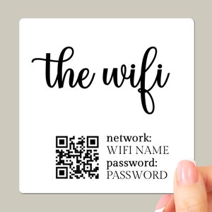 May include: White card with the text "the wifi" in black cursive font. A black and white QR code is below the text. The text "network: WIFI NAME password: PASSWORD" is below the QR code.