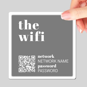 May include: A white square sign with a gray background and the text "the wifi" in white. A black and white QR code is in the lower left corner with the text "network NETWORK NAME" and "password PASSWORD" below it.