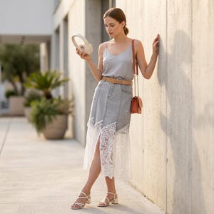 Può includere: Un top a canotta grigio chiaro abbinato a una gonna in denim effetto vissuto con orlo in pizzo bianco. L'outfit include una cintura in pelle beige, una piccola borsa a tracolla marrone con catena dorata e sandali bianchi con tacco largo.