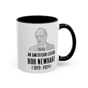 May include: White ceramic mug with a black rim and handle. The mug features a black and white sketch of Bob Newhart and the text "An American Legend Bob Newhart (1929-2024)"