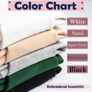 Peut inclure: Un nuancier pr&eacute;sente une pile de sweatshirts brod&eacute;s en blanc, sable, gris sport, vert for&ecirc;t et noir. Le texte "Color Chart" est en haut et "Embroidered Sweatshirt" en bas.
