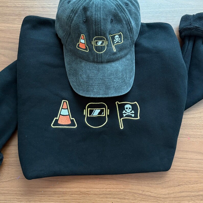 Peut inclure: Un sweat-shirt noir et une casquette de baseball avec les lettres "AOP" et des graphiques. Les motifs comprennent un c&ocirc;ne de signalisation, un masque de soudure et un drapeau de pirate. Les deux articles sont gris fonc&eacute;.