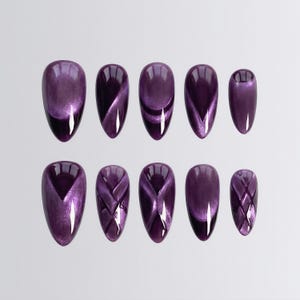 May include: A set of ten purple press-on nails with a glossy finish. The nails are oval-shaped and feature a cat-eye effect, with varying designs including diagonal and crisscross patterns. The nails are arranged on a light gray background.