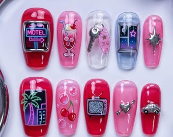 May include: A set of ten press-on nails featuring a pink and red color palette with various designs including a motel sign, a milkshake, a key with a 202 tag, a window, a star, a palm tree, cherries with bubbles, a television, a heart, and a car.