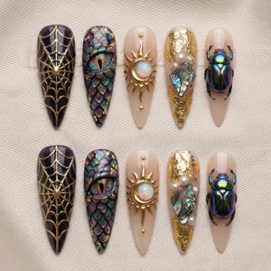 May include: A set of ten stiletto-shaped press-on nails featuring diverse designs including a black spiderweb with gold lines, iridescent dragon scales with a central eye, a gold sun and moon with an opal, gold leaf with pearls, and a metallic beetle.