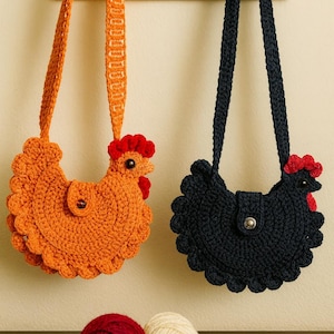 May include: Two crochet chicken-shaped purses, one orange and one navy blue, hang from hooks. The orange purse has a red comb and wattle, and the navy blue purse has red accents. Below are yarn balls and a crochet hook.