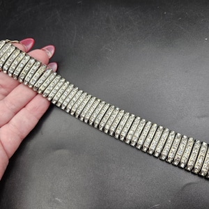 Puede incluir: Un brazalete plateado adornado con filas de pedrería transparente. El brazalete es rectangular y flexible, con un cierre. La pedrería está engastada en un estilo de canal, creando un brillo continuo. El brazalete mide unos 18 cm de largo.