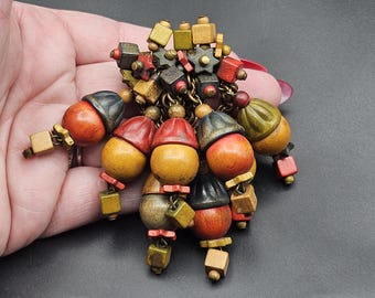 May include: A cluster of wooden beads in various shades of red, orange, yellow, green, and brown, with some metallic accents. The beads are strung together with a metal chain and have a vintage aesthetic.