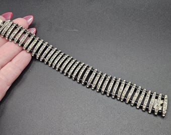 May include: Silver-toned bracelet with a repeating pattern of curved bars, each set with small, clear rhinestones. The bracelet is shown against a dark background, highlighting the sparkle of the stones.