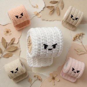May include: A selection of crocheted toilet paper rolls in pastel shades of white, pink, beige, and peach. Each roll has an embroidered angry face. The rolls are arranged on a neutral background with dried flowers and paper scraps.
