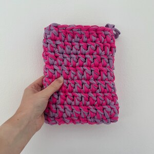 May include: A rectangular crochet pouch crafted from thick fabric yarn in alternating horizontal rows of vibrant hot pink and soft lavender. The textured, chunky stitch pattern creates a dense, durable surface with a small loop at the top corner.