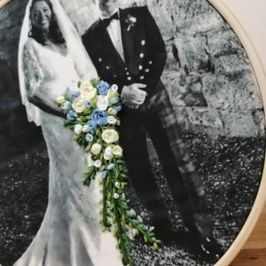 May include: A black and white photo of a bride and groom on their wedding day. The bride is wearing a white dress and a veil. The groom is wearing a suit and tie. The bride is holding a bouquet of embroidered flowers.