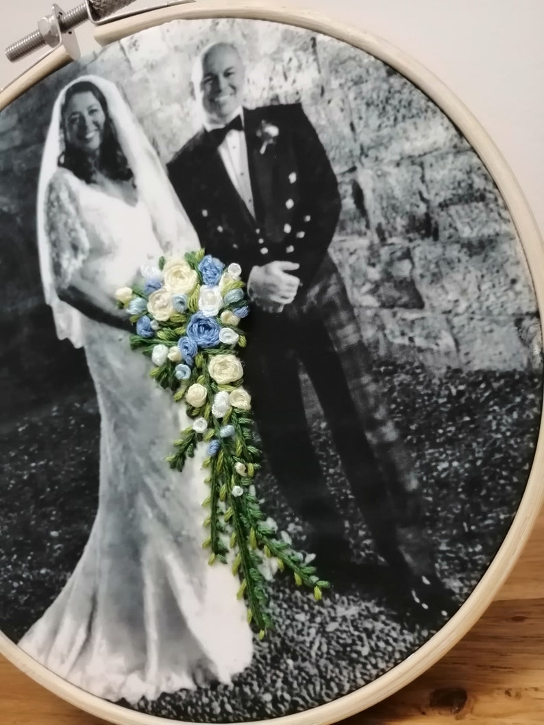 May include: A black and white photo of a bride and groom on their wedding day. The bride is wearing a white dress and a veil. The groom is wearing a suit and tie. The bride is holding a bouquet of embroidered flowers.