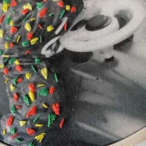 May include: A black and white photo of a person with a colorful embroidery design on the left side of the image. The embroidery is made with red, yellow, and green thread.