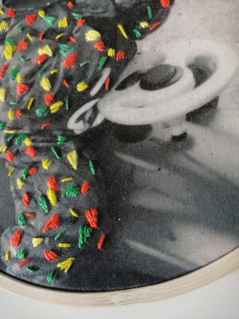 May include: A black and white photo of a person with a colorful embroidery design on the left side of the image. The embroidery is made with red, yellow, and green thread.