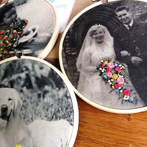 May include: Three embroidered hoop art pieces. The first shows a young Black child wearing a colorful patterned shirt. The second shows a couple in black and white, the woman in a white dress with a bouquet of pink, yellow, and blue flowers. The third shows a black and white photo of a dog.