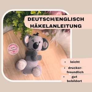 Könnte beinhalten: Gehäkeltes Koala-Amigurumi-Spielzeug mit grauem Fell, weißen Akzenten und einem süßen Ausdruck. Das Bild enthält den Text "DEUTSCH/ENGLISCH HÄKELANLEITUNG" und eine Liste von Merkmalen: "leicht", "druckerfreundlich", "gut bebildert".