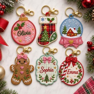 May include: Six embroidered Christmas keychains with gold-tone lobster clasps. Designs include a pink ornament with 'Olivia', a plaid stocking, a snow globe, a gingerbread person, a scalloped tag with 'Sophia', and a wreath with 'Emma'.