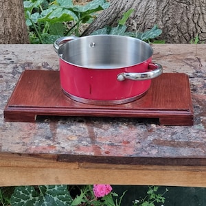 Könnte beinhalten: Ein roter Topf aus Metall mit einem silbernen Griff steht auf einem dunkelbraunen Holztrichter. Der Trichter hat einen erhöhten Rand und ist aus Holz.