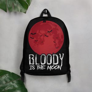 Może przedstawiać: Czarny plecak z nadrukiem czerwonego, pełnego księżyca i nietoperzy z przodu. Pod księżycem znajduje się napis "BLOODY IS THE MOON".