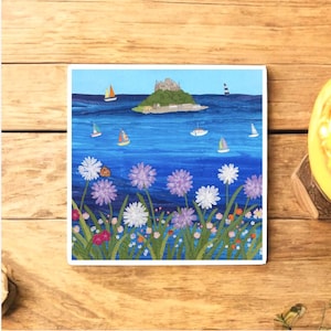 May include: Square art print depicting a coastal scene with a castle on an island, sailboats, and flowers. The artwork uses a blue and green colour palette. The print is set against a wooden background.