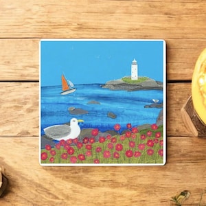 May include: Square artwork showing a coastal scene with a white lighthouse on a rocky island, a sailboat, and a seagull. The foreground features red flowers, and the background is a blue sky and ocean.