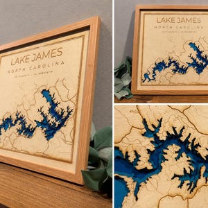 May include: A square wooden framed wall art piece featuring a laser-cut topographic map of Lake James, North Carolina. The map displays deep blue water layers set against a light tan wood background with engraved land contours and coordinates.