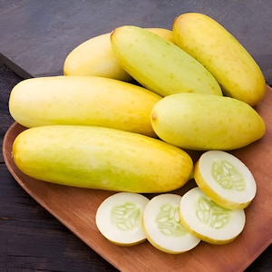 May include: A wooden tray filled with yellow cucumbers. Some of the cucumbers are sliced, revealing the light green flesh and seeds.
