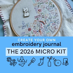 May include: An embroidery hoop with a detailed, colorful stitched design, including the year 2025 and various small icons. A small dog pin is attached. The text "CREATE YOUR OWN embroidery journal THE 2026 MICRO KIT" is displayed below.