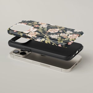 May include: A black phone case with a floral pattern featuring pink and white roses on a dark background. The case is shown separated from a black phone case and a gold phone.