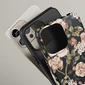 May include: A black phone case with a floral design featuring pink roses and green leaves on a black background. The case is shown with a clear phone case and a black phone case.