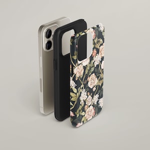 May include: A black phone case with a floral pattern of pink roses and white flowers on a dark background. The case is shown next to a gold phone.