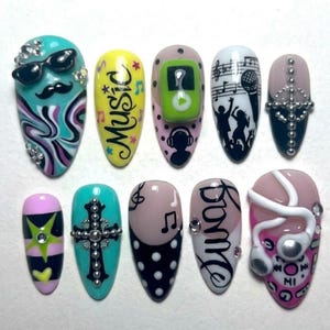 May include: A set of ten press-on nails featuring music-themed designs including a mustache with sunglasses, the word Music, a green music player, silhouettes of people dancing, a cross with silver studs, musical notes, and white headphones.