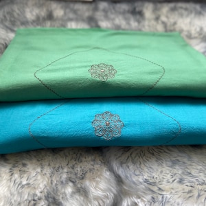 May include: Two prayer rugs, one green and one blue, with embroidered floral designs. The rugs are folded and stacked on top of each other.