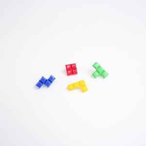 May include: Four colorful plastic Tetris-shaped blocks on a white background. The blocks are red, blue, green, and yellow.