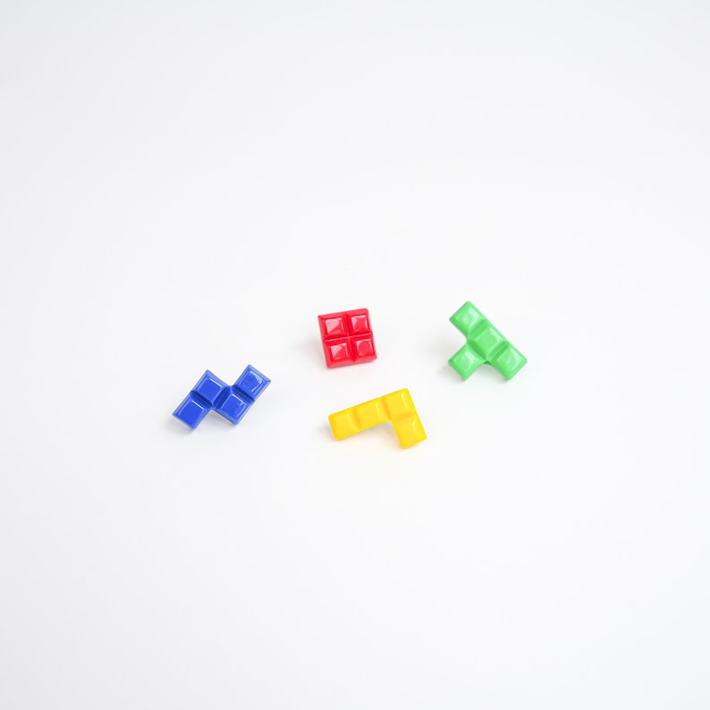 May include: Four colorful plastic Tetris-shaped blocks on a white background. The blocks are red, blue, green, and yellow.