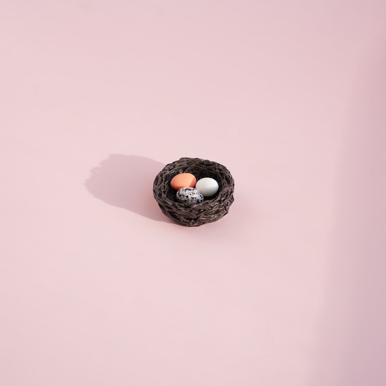 May include: A small brown woven nest with three eggs inside. One egg is white, one is speckled brown and white, and one is light orange.