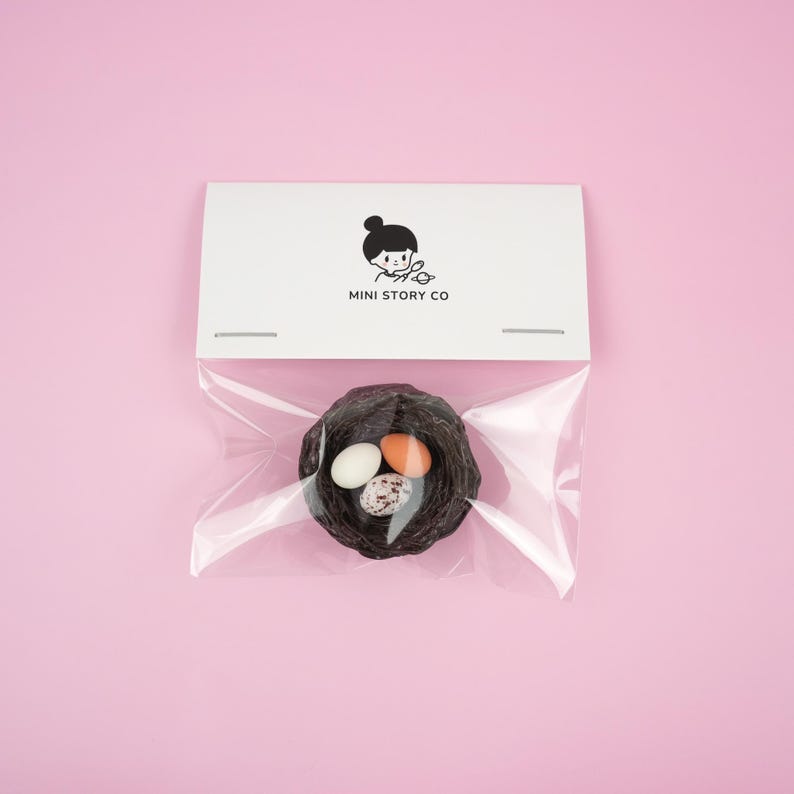 May include: A small brown bird's nest with three speckled eggs inside, packaged in a clear plastic bag with a white card that says "MINI STORY CO" on it.