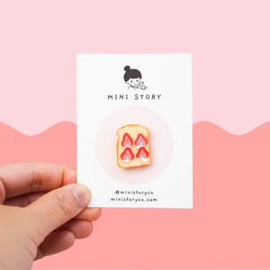 Pode incluir: Um cartão branco com o texto "MINI STORY" e um pequeno cartão branco com o texto "@ministoryco ministoryco.com". O cartão apresenta uma miniatura de fatia de pão branco com fatias de morango vermelhas no topo.