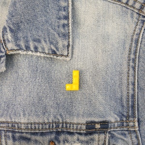 May include: A yellow plastic letter L pinned to a blue denim jacket.